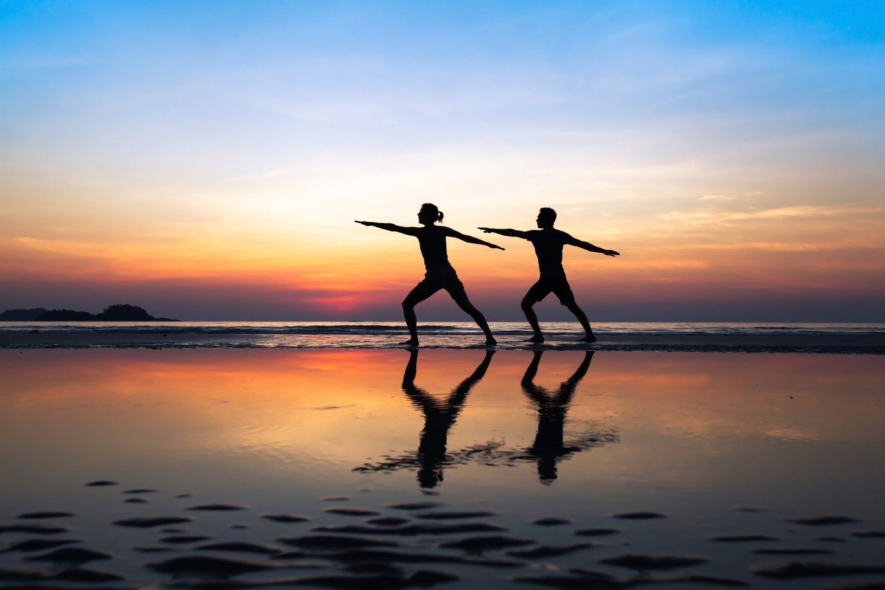 Two people doing yoga on a beach at sunset
